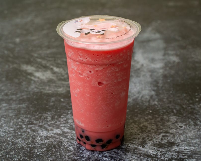 A vibrant pink bubble tea with black tapioca pearls sits on a dark, textured surface.