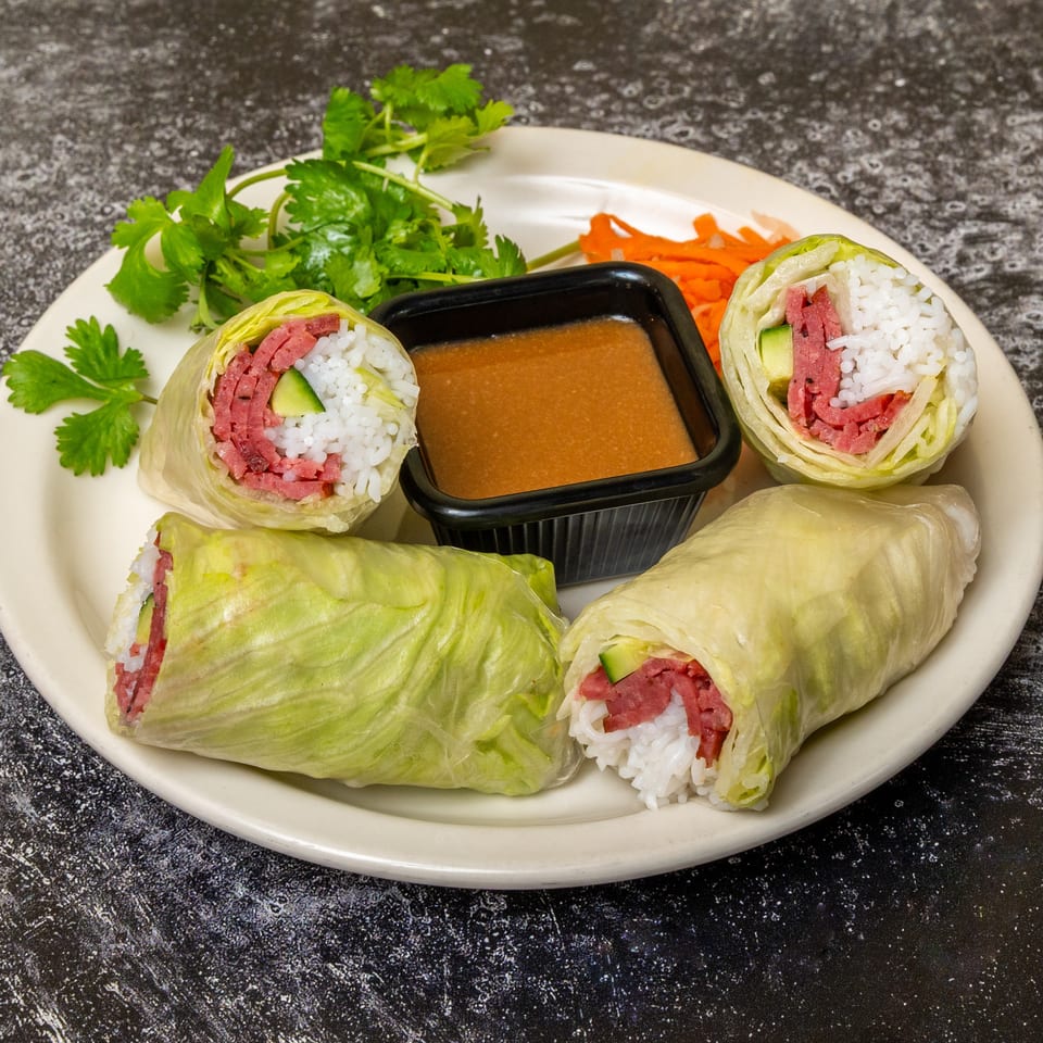 Four fresh spring rolls with corned beef, rice, and cucumber, served with peanut sauce and cilantro.
