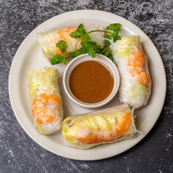 Four fresh spring rolls with shrimp, vermicelli, and lettuce, served with a side of peanut sauce.