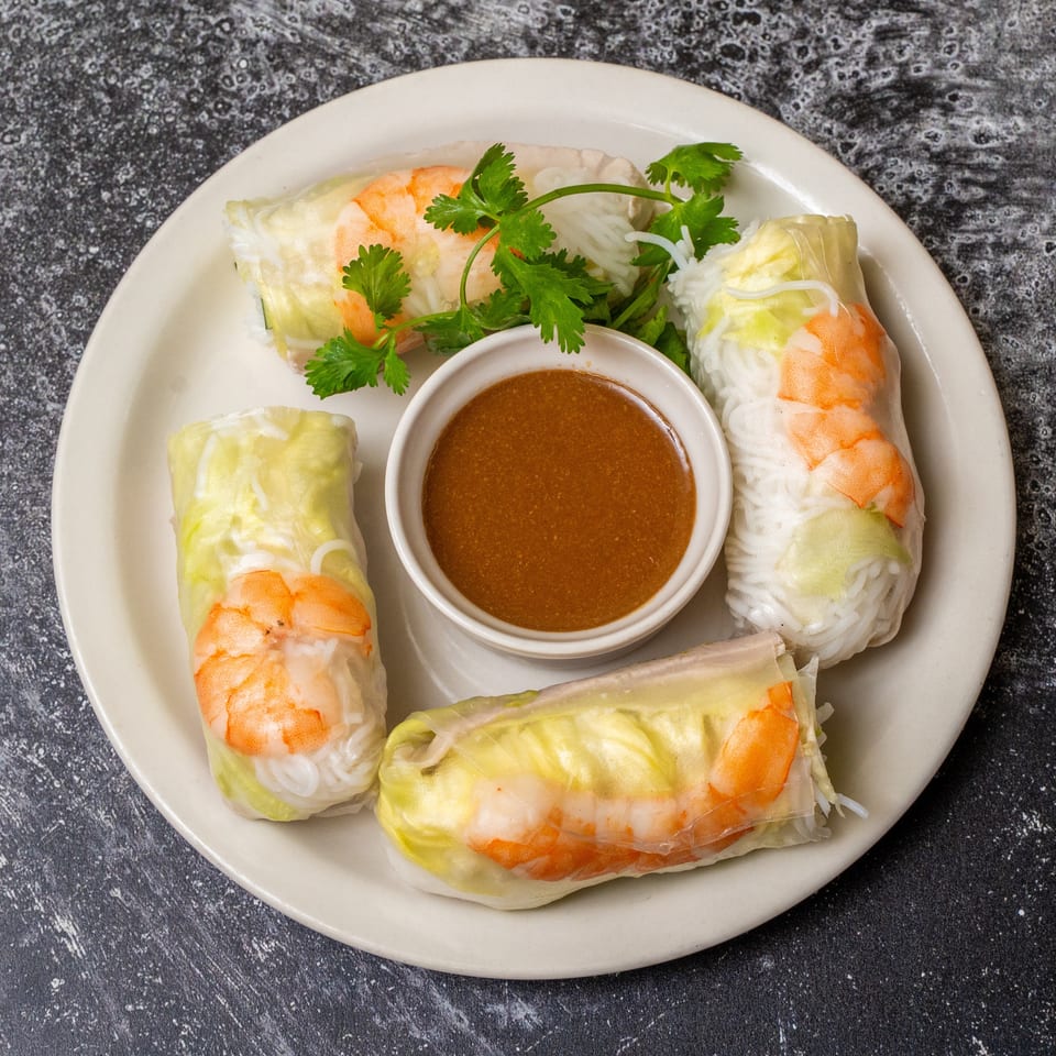 Four fresh spring rolls with shrimp, vermicelli, and lettuce, served with a side of peanut sauce.