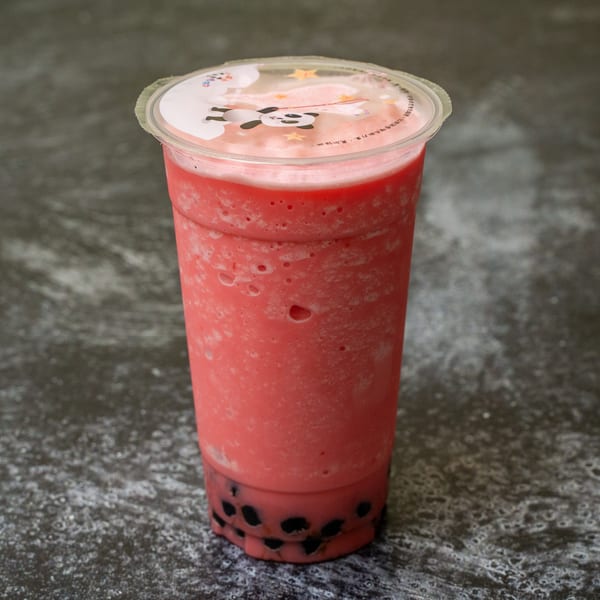 A vibrant pink strawberry boba tea with black tapioca pearls sits on a dark, textured surface.